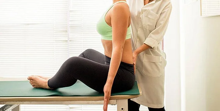 Fisioterapeuta avaliando a postura da coluna de uma paciente sentada